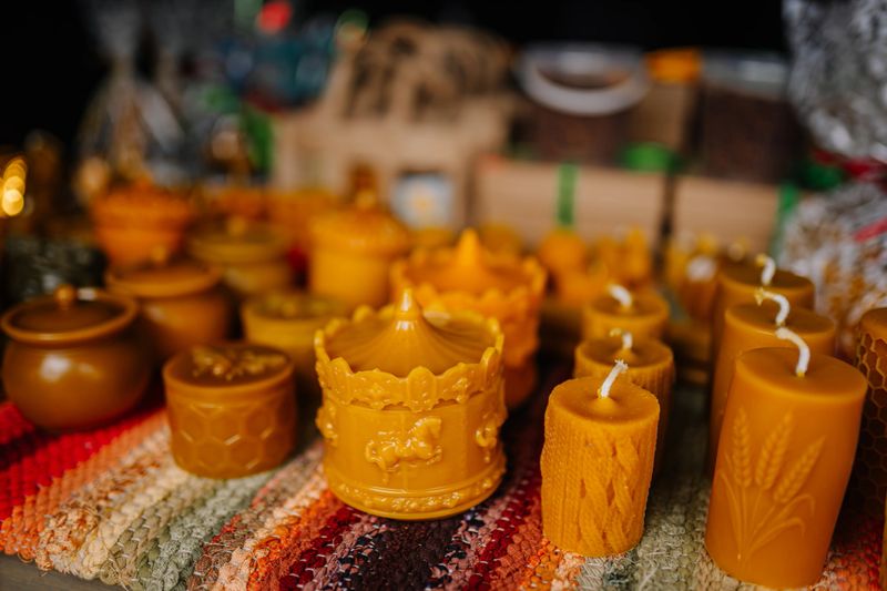 Handcrafted yellow candles and decorative containers are beautifully arranged on a colorful woven mat, creating a warm and inviting atmosphere for home decor