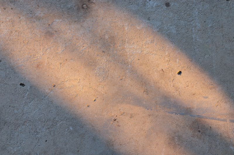 A minimalist shot of sunlight hitting a cement surface, highlighting the gritty texture and warm tones of the ground