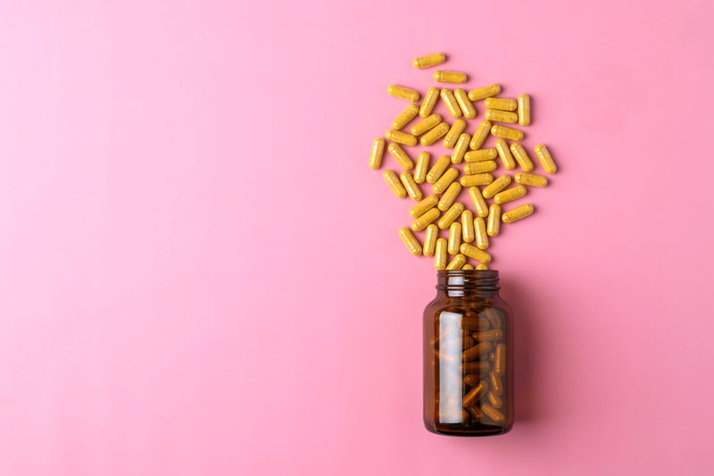 Minimal wellness banner shows yellow supplement capsules rising from amber glass bottle on bright pink background with copy space.