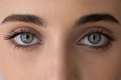Close-up of greenish eyes with long eyelashes and well-groomed eyebrows.
