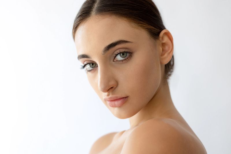 Natural beauty portrait of a young woman with minimal makeup, healthy glowing skin and green eyes on white background.