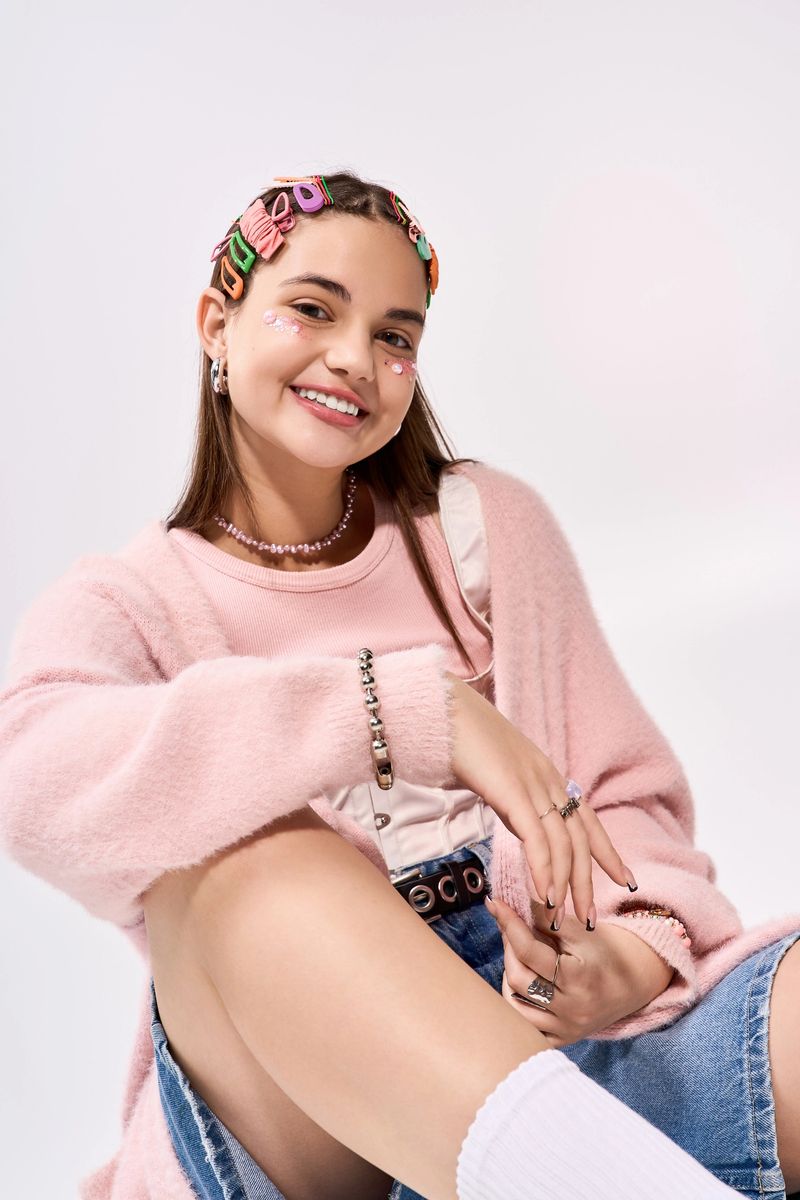 A trendy teenage girl showcases her vibrant winter style in a soft pink cardigan while smiling.