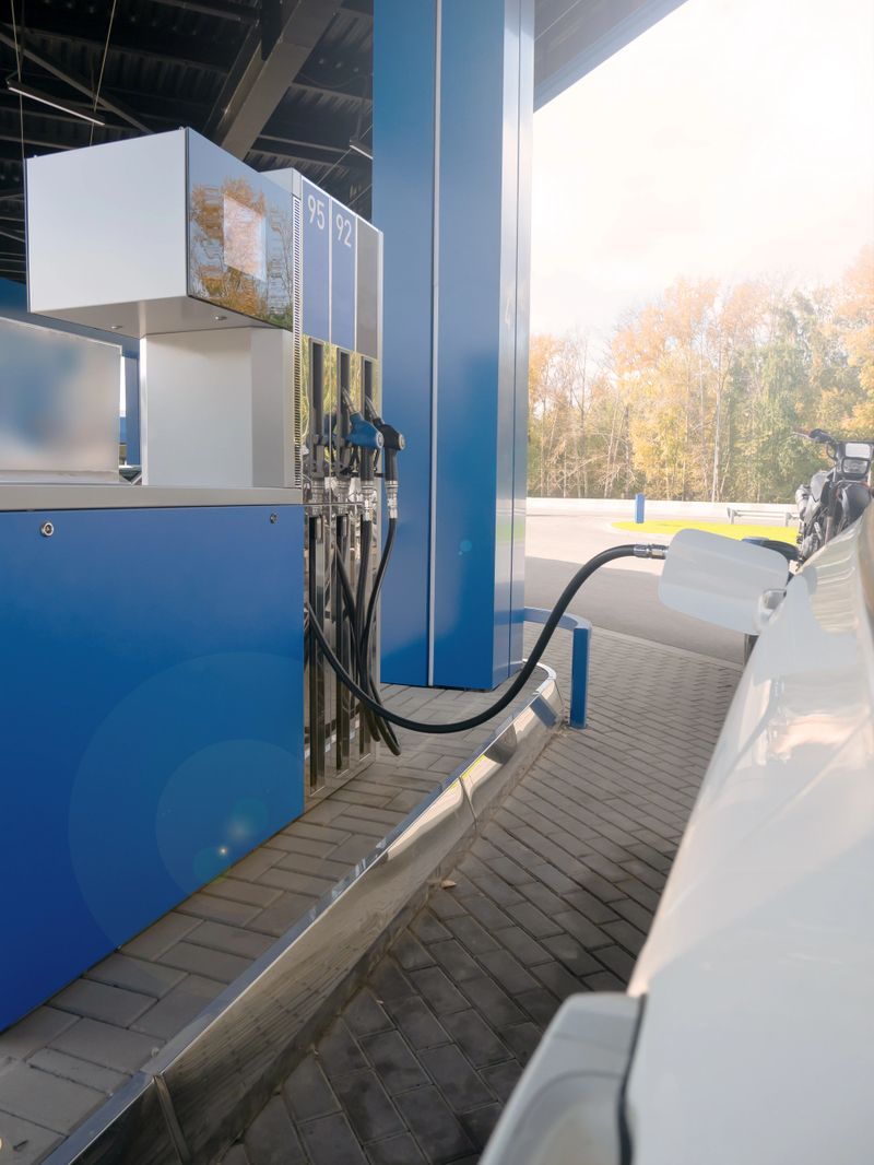 White car refuels at modern gas station with blue pump. Fueling vehicle energy demand and transportation concept.