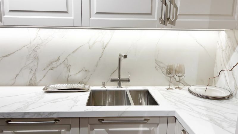 Stylish modern kitchen interior with white marble countertop, double sink, sleek cabinets, under lighting.
