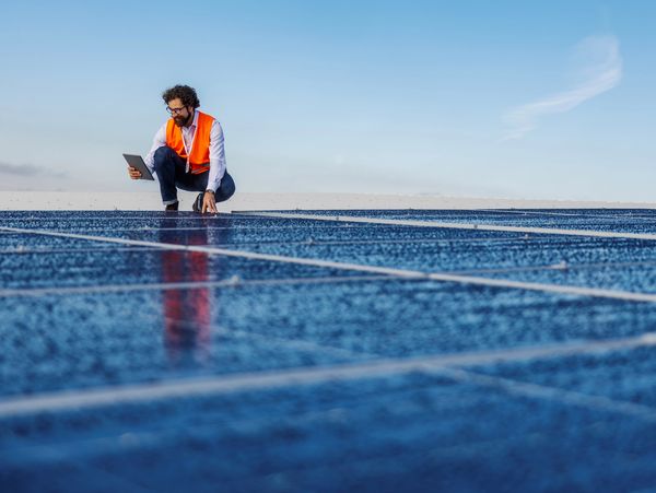 Hombre con chaleco naranja inspecciona paneles solares.