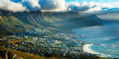 Coastal city by mountains and ocean under cloudy sky.