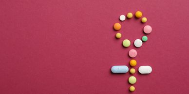 Pills arranged in the shape of the female gender symbol on a red background.