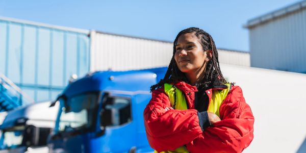 Woman in red safety jacket standing in front of trucks.