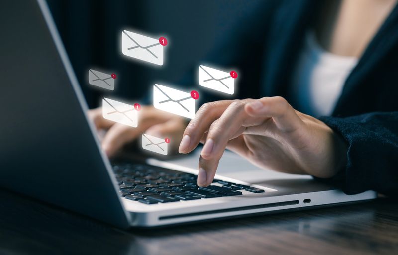A professional typing on a laptop with floating email notification icons, representing digital communication, email marketing, online messaging, business notifications, and modern workflow technology.