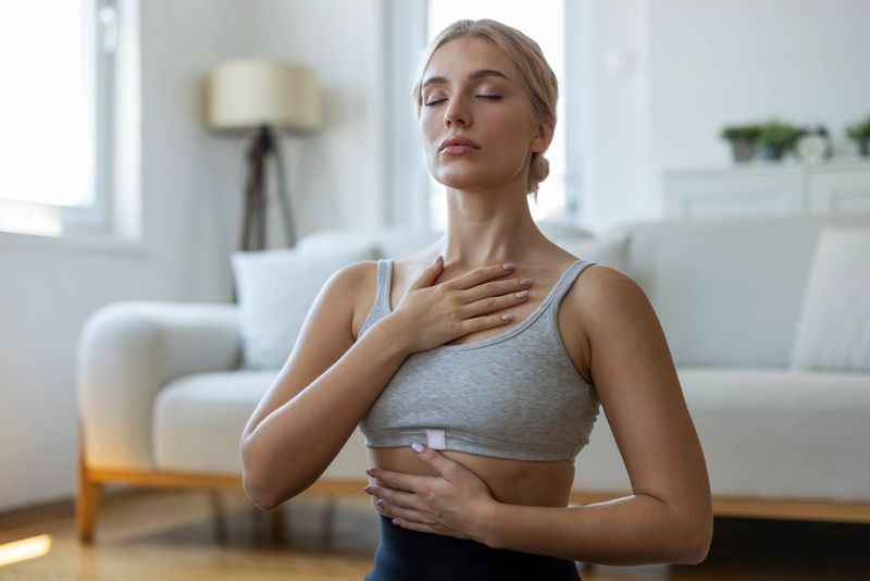 Woman practicing conscious breathing and mindfulness exercise at home with hands on chest and abdomen. Concept of stress relief, emotional balance, mental wellbeing and relaxation in a calm indoor environment.