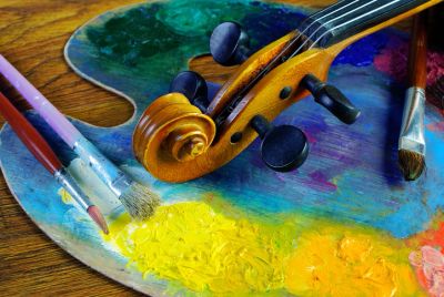 Violin on colorful artist palette with paintbrushes.