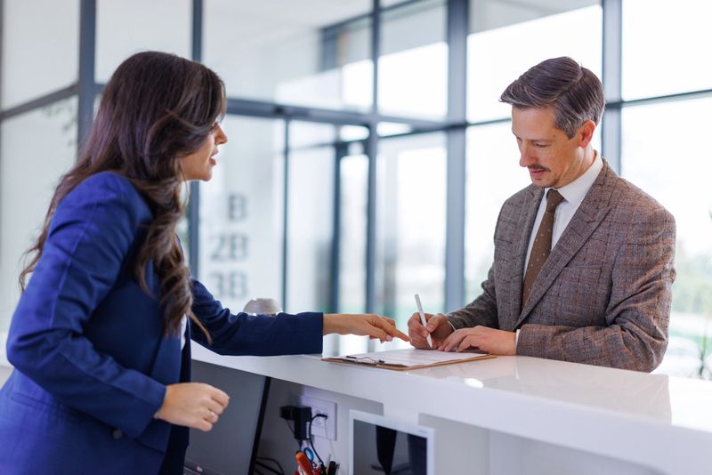Businesswoman interacting with client signing paperwork at an office reception desk