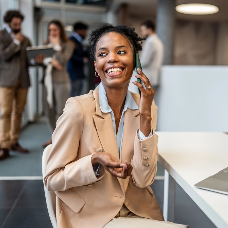 Happy black businesswoman talking on smartphone in a modern office, enjoying communicating with colleagues and clients