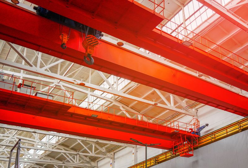 Overhead crane. Red Crane Operates in Spacious Industrial Warehouse During Bright Daylight. Gantry crane. Gantry crane with hook for lifting, moving heavy cargo. Granularity, blurred focus.