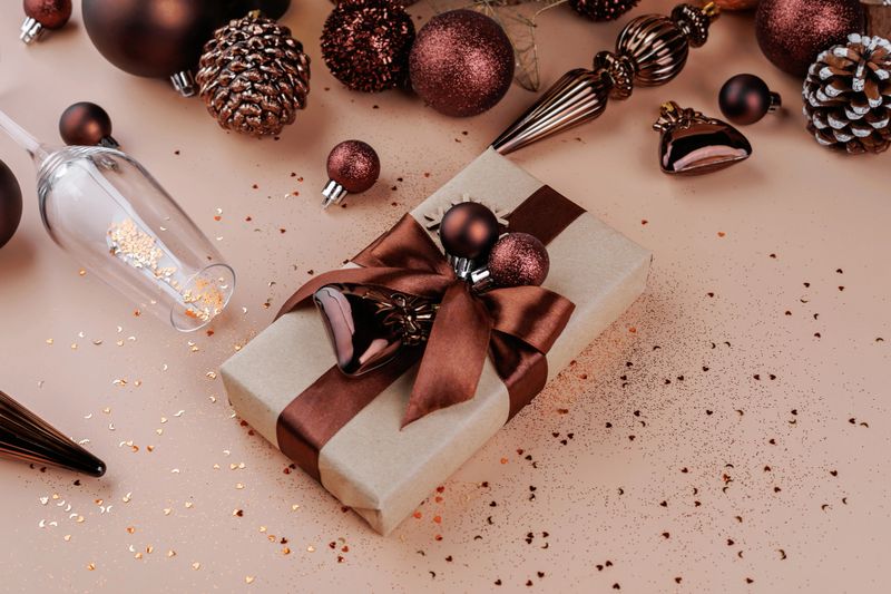 Gift box with bronze ribbon and Christmas baubles surrounded by holiday decor and glitter