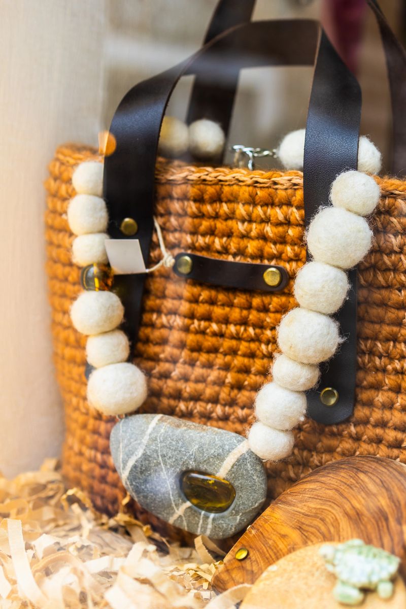 Handcrafted wool necklace with stone pendant on wicker bag. Natural materials, rustic fashion, and boho accessory design in artisan boutique display
