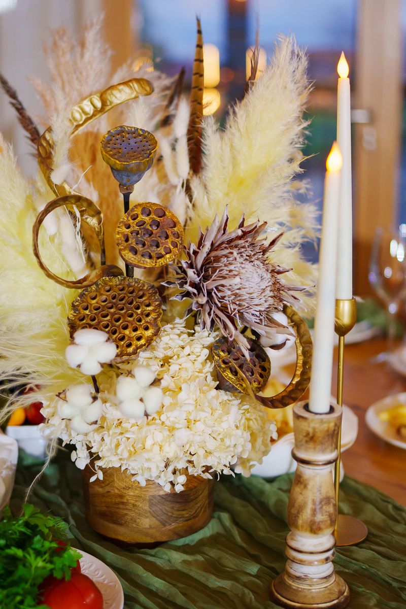 A stunning floral centerpiece featuring dried blooms and natural elements sits on a table. Elegant candles add warmth to the setting, enhancing the cozy atmosphere.