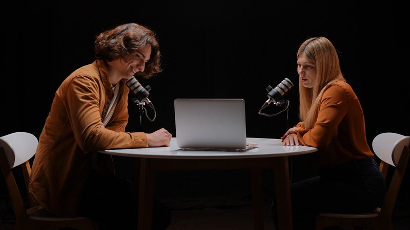 An intimate podcast recording session takes place in a sleek studio, where two influencers share insights around a round table, bringing their stories to life through shared dialogue.
