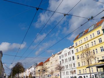 Sunny day with buildings and overhead tram wires.