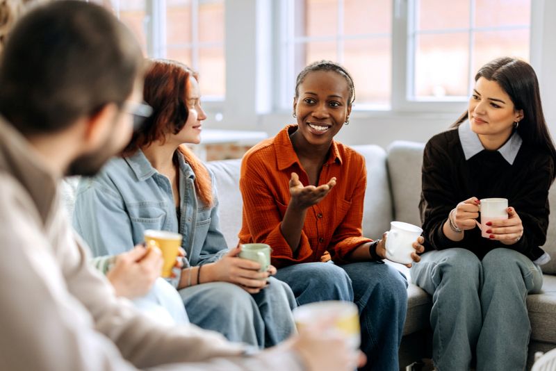 A group of cheerful colleagues relax in the office break room, sitting on a sofa and engaging in a casual conversation during their break.