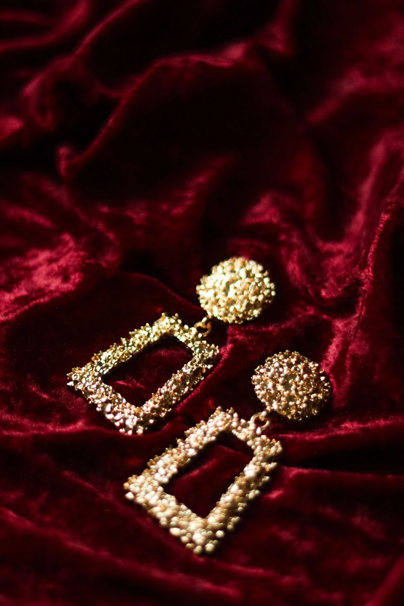 Gold textured dangle earrings resting on a luxurious red velvet fabric, showcasing fashion accessory design and elegance