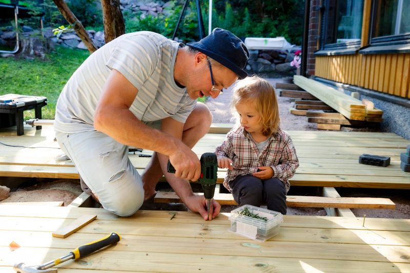 Joyful father and daughter building a wooden patio deck together. Authentic family DIY home improvement project, sunny outdoor leisure. High quality photo