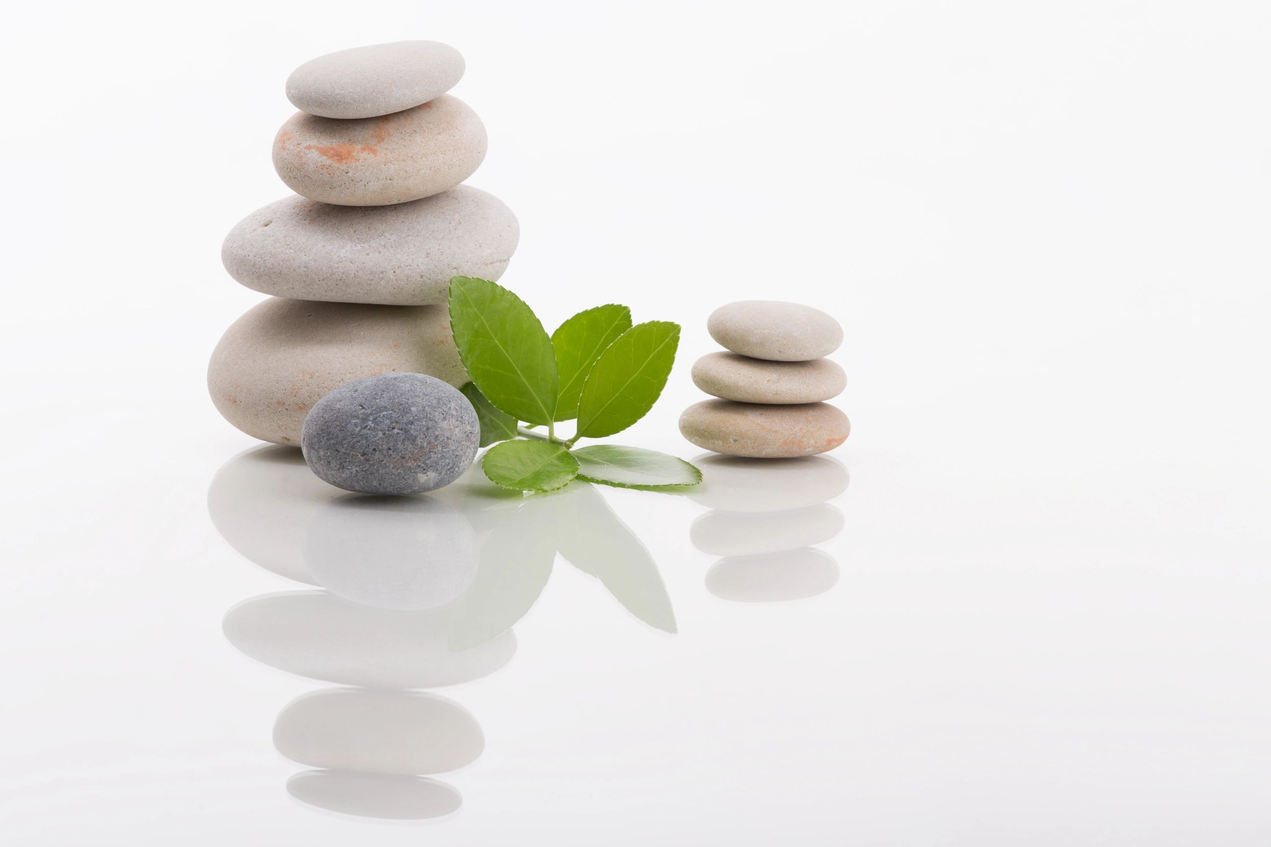 Stacked smooth stones with green leaves on a reflective white surface.