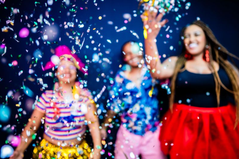 Close-up of colorful confetti scattered in the air, and in the background people celebrating a carnival - Studio Shot