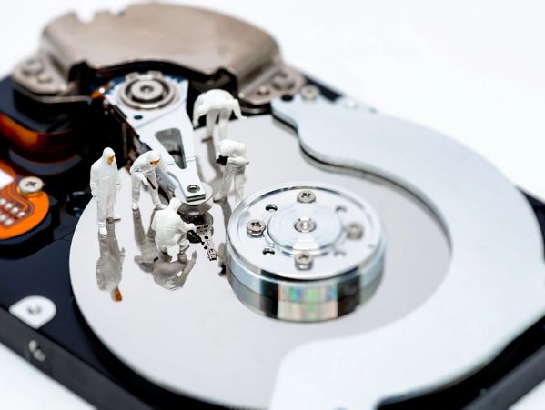 Miniature figures working on a hard drive's reflective surface.