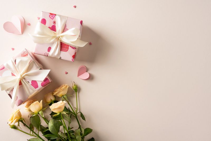 Romantic scene with pink gift boxes tied with white ribbons and pale roses placed on a soft beige background, conveying Valentine celebration and greeting with warm mood and gentle love