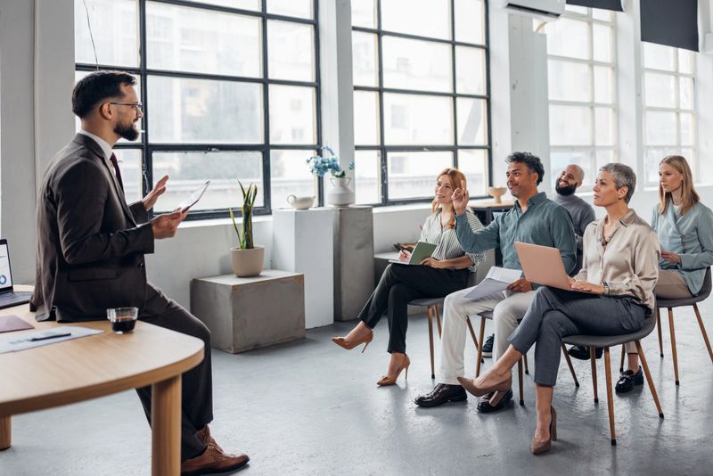 A speaker shares ideas with an engaged audience, fostering interaction and discussion in a bright and contemporary meeting space designed for learning and sharing valuable insights.