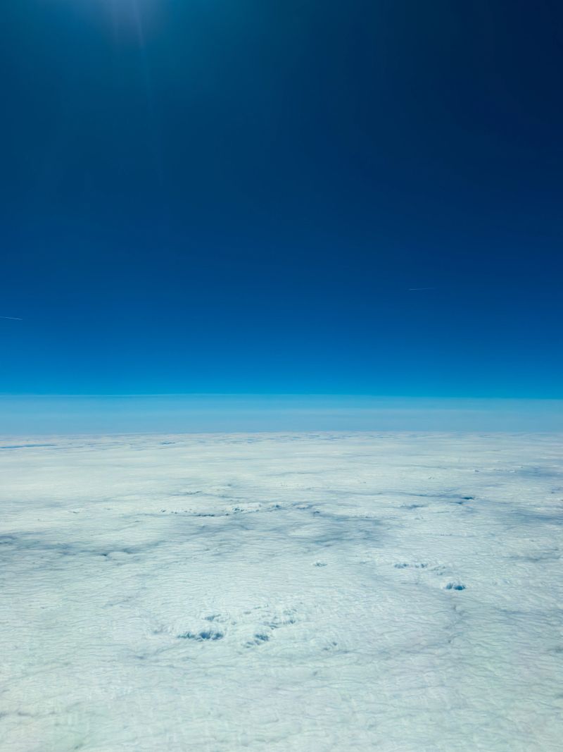 Fluffy white clouds blanket the earth below, while a vibrant blue sky frames the scene high above, creating a peaceful atmosphere during an aerial journey.
