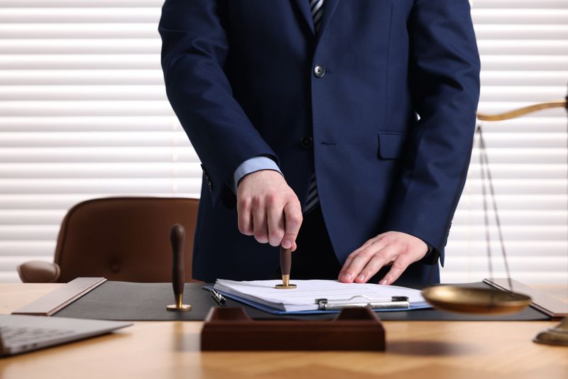 Notary stamping document at table in office, closeup