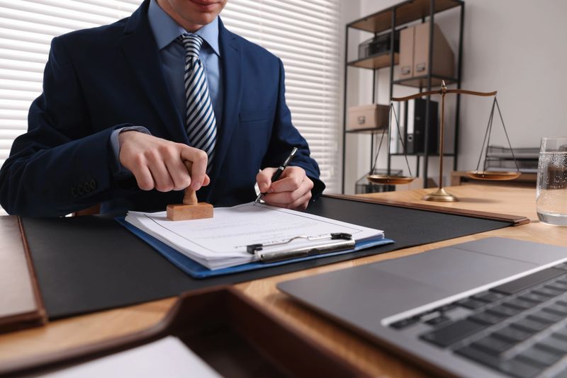 Notary with pen stamping document at table in office, closeup