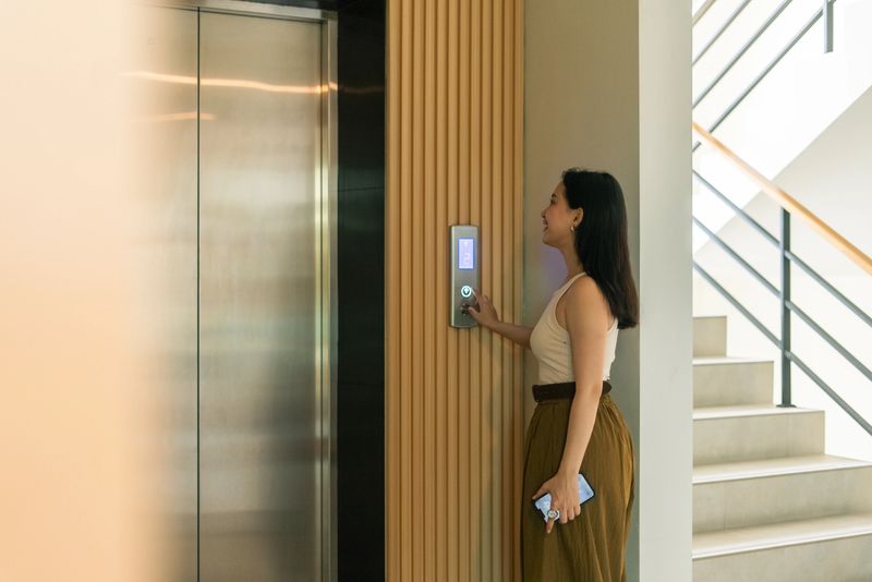 Woman standing in building hall, pressing elevator button, going to work or returning home
