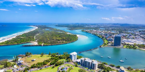 Aerial view of a coastal city with a river, island, and buildings under a blue sky.
