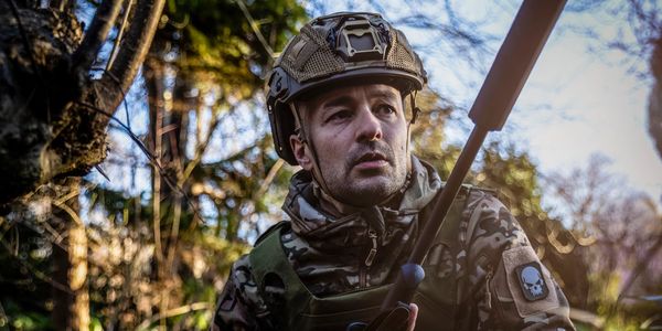 Soldier in camouflage gear crouching in the forest.