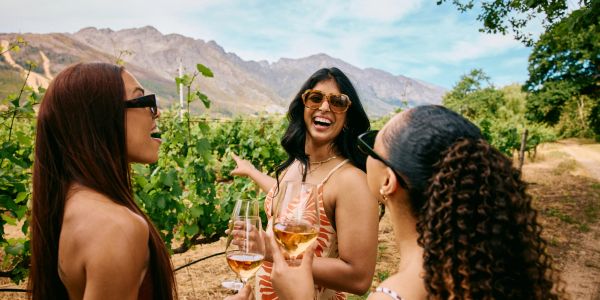 Three women enjoying wine outdoors in a vineyard.