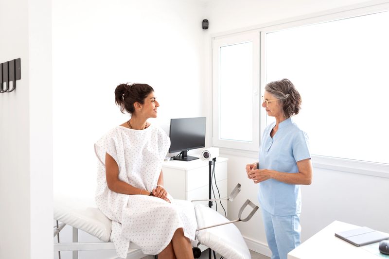 Mature female gynecologist in consultation with a young female patient preparing for a gynecological check-up on the examination table in the doctor's office - Buenos Aires - Argentina