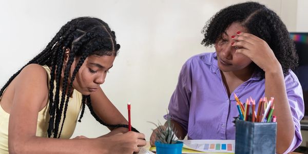 A young girl studies while a woman looks on supportively.