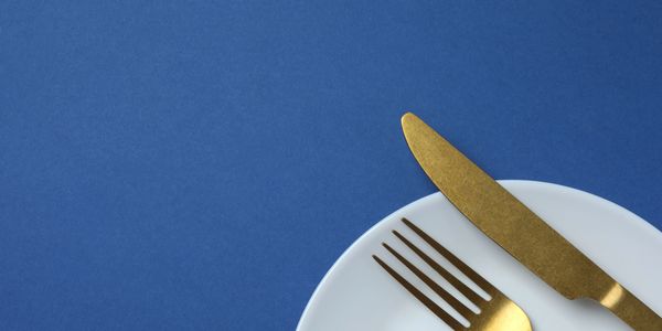 Golden fork and knife on a white plate with blue background.