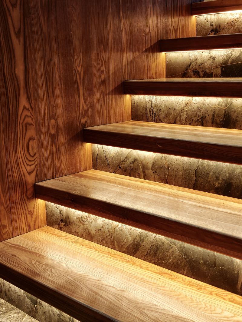 A modern, straight wooden staircase with under-tread lighting and a natural wood texture. Ideal for home and real estate interior design. Background.