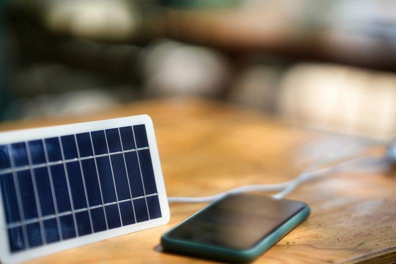 Compact solar charger supplying energy to a smartphone placed on a wooden surface.