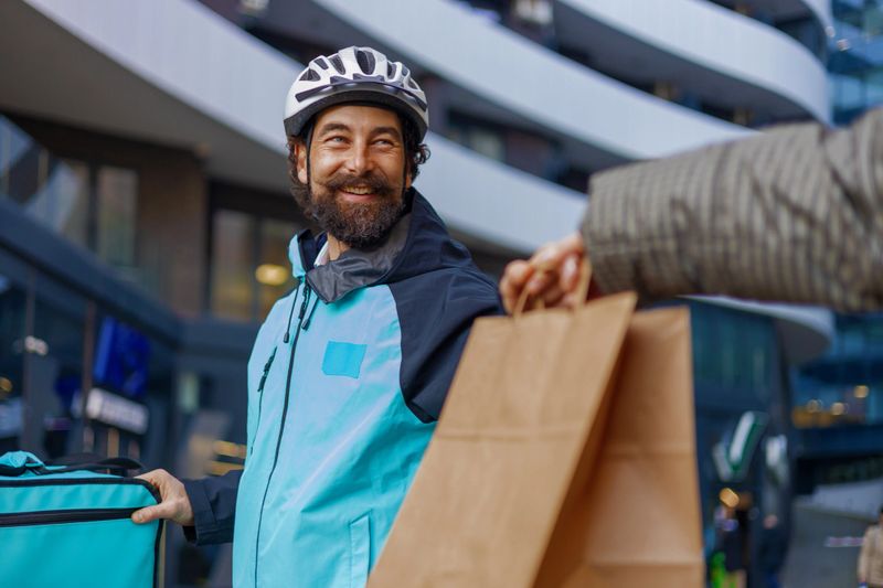 Delivery courier giving a package during a city delivery, smiling while wearing protective helmet. Concept of fast shipping, customer service, and modern logistics industry.