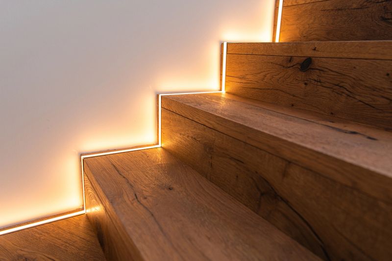 Wooden stairs lead up with light strips along the edges in a modern home. Warm light enhances the design.