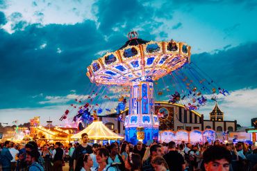 A brightly lit swing ride at a bustling carnival during twilight.