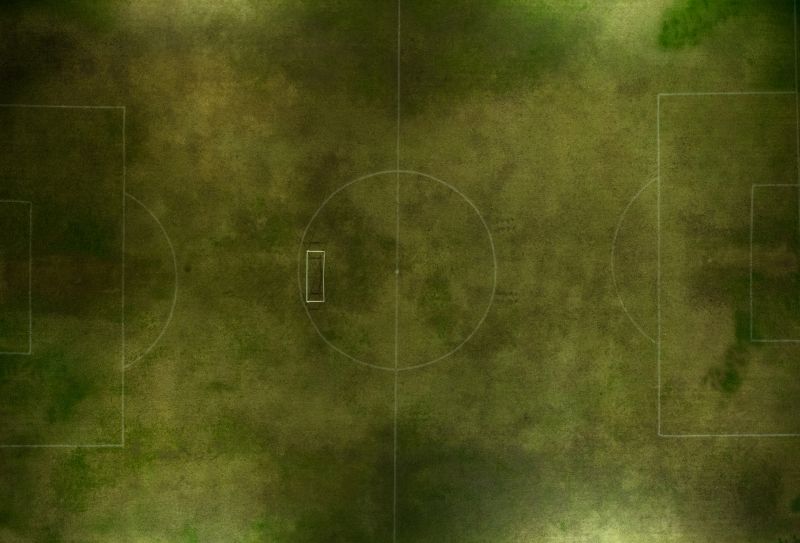 Top-down drone shot of a green soccer field showing the center circle and goal areas. The empty pitch conveys sport, training, and outdoor recreation in natural light.
