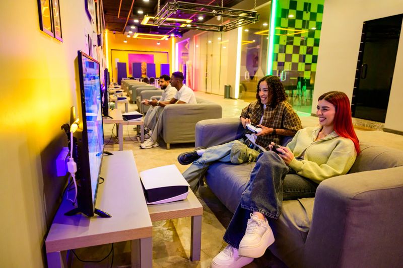 Group of young adult friends enjoying multiplayer video games together on consoles in a modern gaming lounge with vibrant neon lighting, sharing a fun and engaging social experience