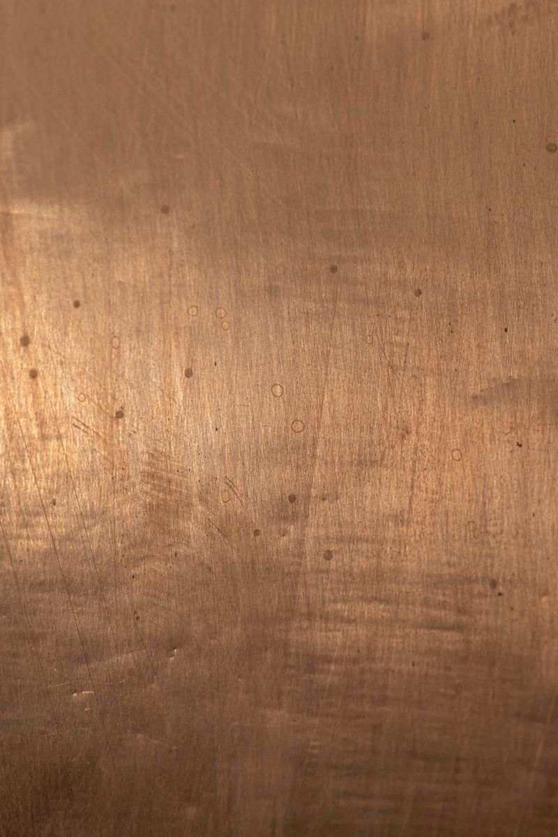 A close-up of a copper toned brushed metal sheet featuring small circular marks and subtle scratches. The warm, rustic texture makes it ideal for backdrops, product showcases or industrial design