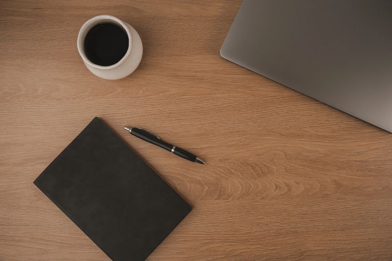 A clean and inviting workspace features a laptop, a coffee cup, and a notebook, creating an ideal environment for studying at home. The warm wood surface enhances focus and comfort
